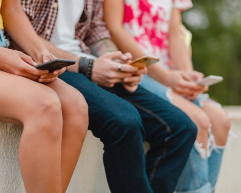 happy young company of smiling friends sitting park using smartphones, man and women having fun together, colorful summer hipster fashion style, communication wireless connecting devices