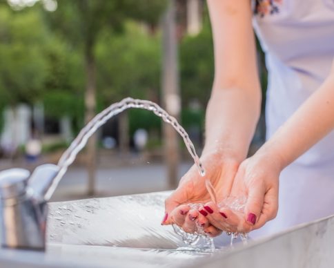 healthy and natural water fountain. Young woman drinking water at the public street fountain on a sunny day in the town square