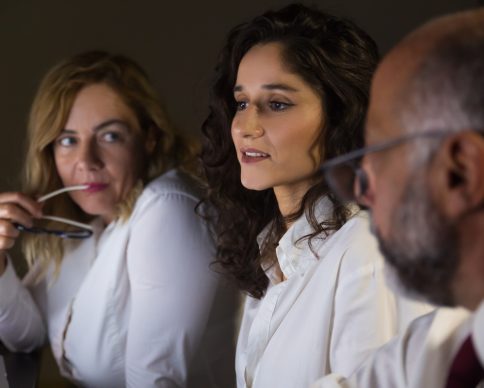 Businessman and businesswomen in dark office. Close-up view of professional male and female business people sitting at workplace and discussing project in dark office. Working late concept