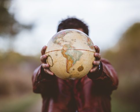 A closeup shot of a male wearing a leather jacket holding a globe in front of him with a blurred background