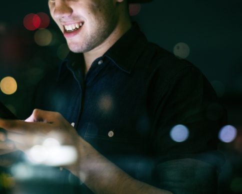 Happy young adult male using a smartphone in a night cityscape