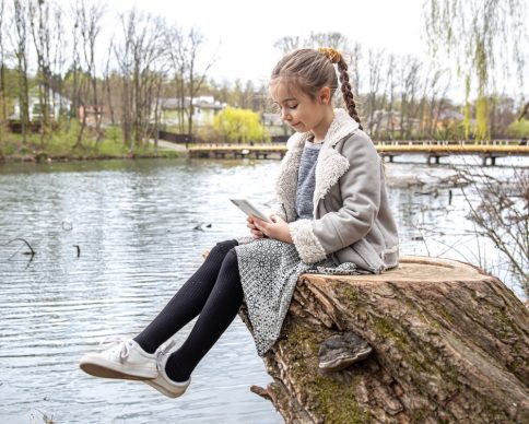 A little girl checks her phone, sitting by the river, and does not pay attention to the nature around. SSUCv3H4sIAAAAAAAACpyRwW7DIAyG75P2DhHnRkoDycRepdrBAdqgUaiAdJqqvvsMhIrzbviz/du/eby/dR1ZIGhBPrtHijDWxmwheojaWcTDYedeWal8S+6ezkMLlNTReQ2mhQtEsVq4KoR2MybhZ06SECFuQYU0fUcCorqgRoEvibLiqcRdTeQkdmCKkEPDwrZkVlER/1dneXxVN3BRVvzmhRsjXhkFxciplJLvn6j8tbUGm9SucXV3AkwqoI3SzWuh7aVpc3HNZ69twm02+rTCa3NinLvBYtKJz6ipKl8hBCyXlTeDBH6yuzZzrIvZwK5KJP5ECo90nBmfOecDp9NI6XEvKL+3atTJ61QhjMW3lq11nTYgbJzkBONHP/DzuWdskj2fGeuVonKQFBiVDA///AMAAP//AwBthNRZmAIAAA==