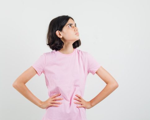 Little girl looking up with hands on waist in pink t-shirt and looking focused , front view.