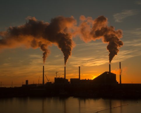 A low angle shot of a factory with smoke and steam coming out of the chimneys captured at sunset