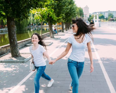 two-girls-holding-hands-walking-pavement